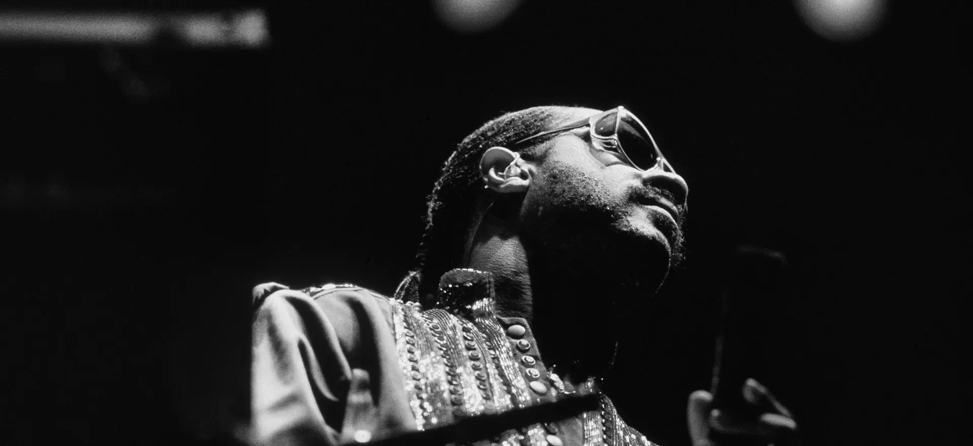 Close-up image looking up at Stevie Wonder performing live at Wembley Arena 1984 – black & white, moody